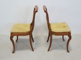 two wooden chairs with yellow upholstered seats against a white wall