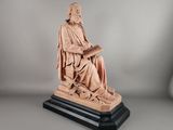 une statue représentant un homme assis sur une chaise en train de lire un livre