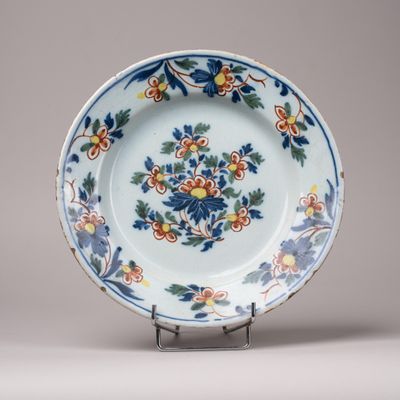 assiette décorée de fleurs et de feuilles, posée sur un socle, sur fond gris