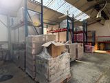 Les cartons sont empilés sur des palettes dans un entrepôt surmonté d'une verrière.
