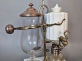une cafetière en verre avec une poignée en laiton posée sur un socle en marbre