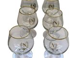 six verres transparents à bord doré sont alignés sur une surface blanche