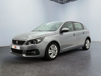 Une voiture argentée est garée dans une pièce blanche au sol noir.