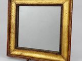 un miroir à cadre doré posé sur un socle en bois, sur fond gris