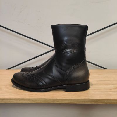des bottes en cuir noir posées sur une étagère en bois devant un mur blanc