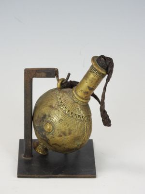 une petite bouteille en laiton munie d'une anse et posée sur un socle