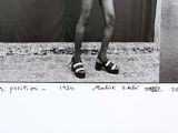 black and white photograph of a man in shorts and sandals holding a tennis racquet