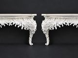 a pair of white carved console tables on a black background