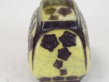 a yellow vase with black flowers on it on a white surface