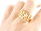 a person ' s hand holding a gold ring with a design on it
