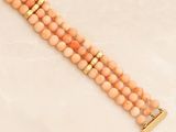 a close up of a peach beaded bracelet with a gold clasp
