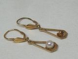 une paire de boucles d'oreilles dorées ornées de perles, posées sur un fond blanc