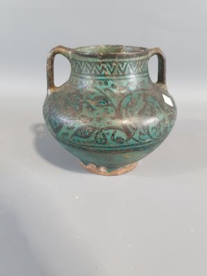 un vase vert posé sur une table, sur fond blanc