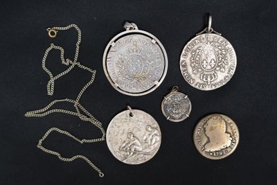 several different types of silver coins and pendants on a black surface