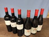 six bottles of red wine lined up on a wooden table