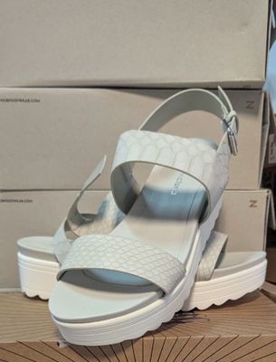 une paire de sandales blanches posée sur une table, avec des cartons en arrière-plan