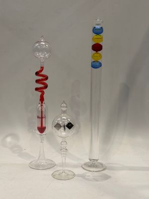 trois vases en verre de couleurs différentes posés l'un à côté de l'autre sur une surface blanche