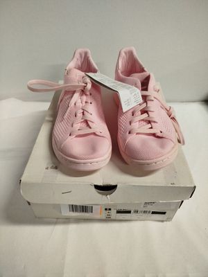 des baskets roses dans une boîte posée sur un lit, avec une étiquette de prix