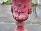 un vase rouge orné d'un visage, posé sur le trottoir