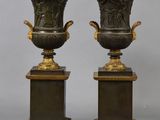 pair of antique bronze vases on pedestals on a gray background