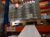 Des cartons sont empilés sur des palettes dans un grand entrepôt, avec des palettes au premier plan