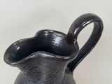 a black vase with a curved handle on a table