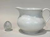 a white pitcher sitting next to an egg on a table
