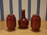 three red vases sitting on top of a wooden table next to a striped wall