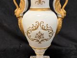 a white and gold vase on a stand on a black background