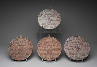 trois médailles de bronze portant des noms, exposées sur un fond gris