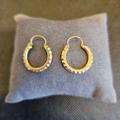 des boucles d'oreilles créoles plaquées or posées sur un coussin gris