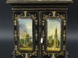un meuble ancien peint en noir et or, orné d'un tableau sur la porte