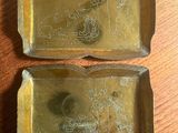 deux plateaux en laiton posés sur une table en bois, sur lesquels est représenté un tableau