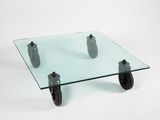 a glass table with wheels on it on a white surface