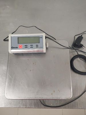 une balance numérique posée sur une surface métallique, avec un cordon