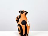 un petit vase orange et noir posé sur une table blanche