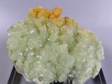 a piece of green and yellow mineral on a clear base