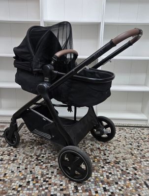 a black stroller with a baby in it sitting on a tiled floor