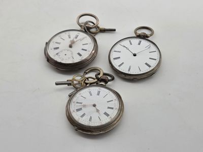 three silver pocket watches with roman numerals on them on a white surface