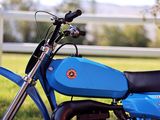 a blue dirt bike parked in the grass by a fence