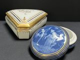 two blue and white porcelain boxes with gold trims on a black surface