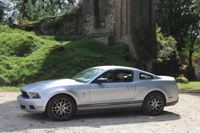 a silver mustang parked in front of a castle