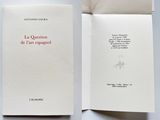 un livre ouvert posé sur une table blanche, à côté d'une feuille de papier