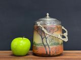 a green apple next to a jar with a painting on it