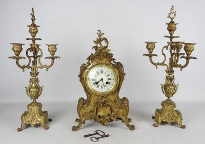 trois bougeoirs dorés et une horloge posés sur une table