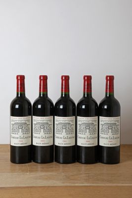 six bouteilles de vin sont posées sur une table en bois devant un mur blanc