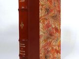 an old book with a red cover sitting on top of a white surface