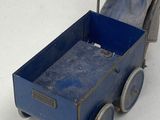 doll in blue dress pushing a blue toy wagon on a white surface