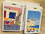 two folders with paintings on them sitting on a wooden table