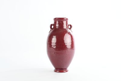 un vase rouge posé sur une surface blanche